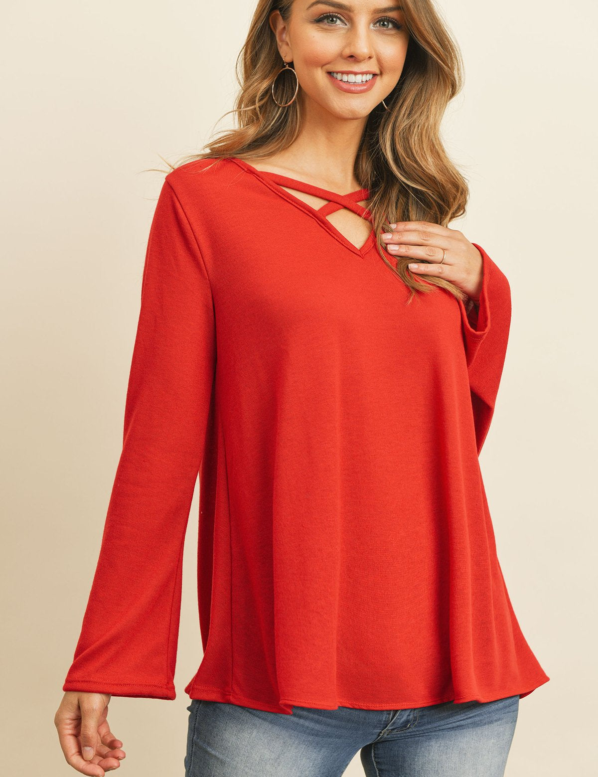 Model wearing Evanthira Criss-Cross Knit Top in red with bell sleeves and criss-cross neckline, paired with jeans.