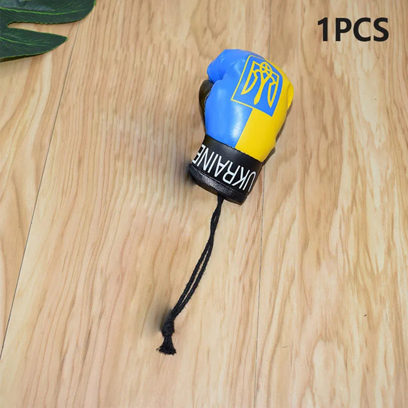 Ukraine flag boxing glove keychain on wooden surface, featuring blue and yellow colors with Ukrainian emblem.