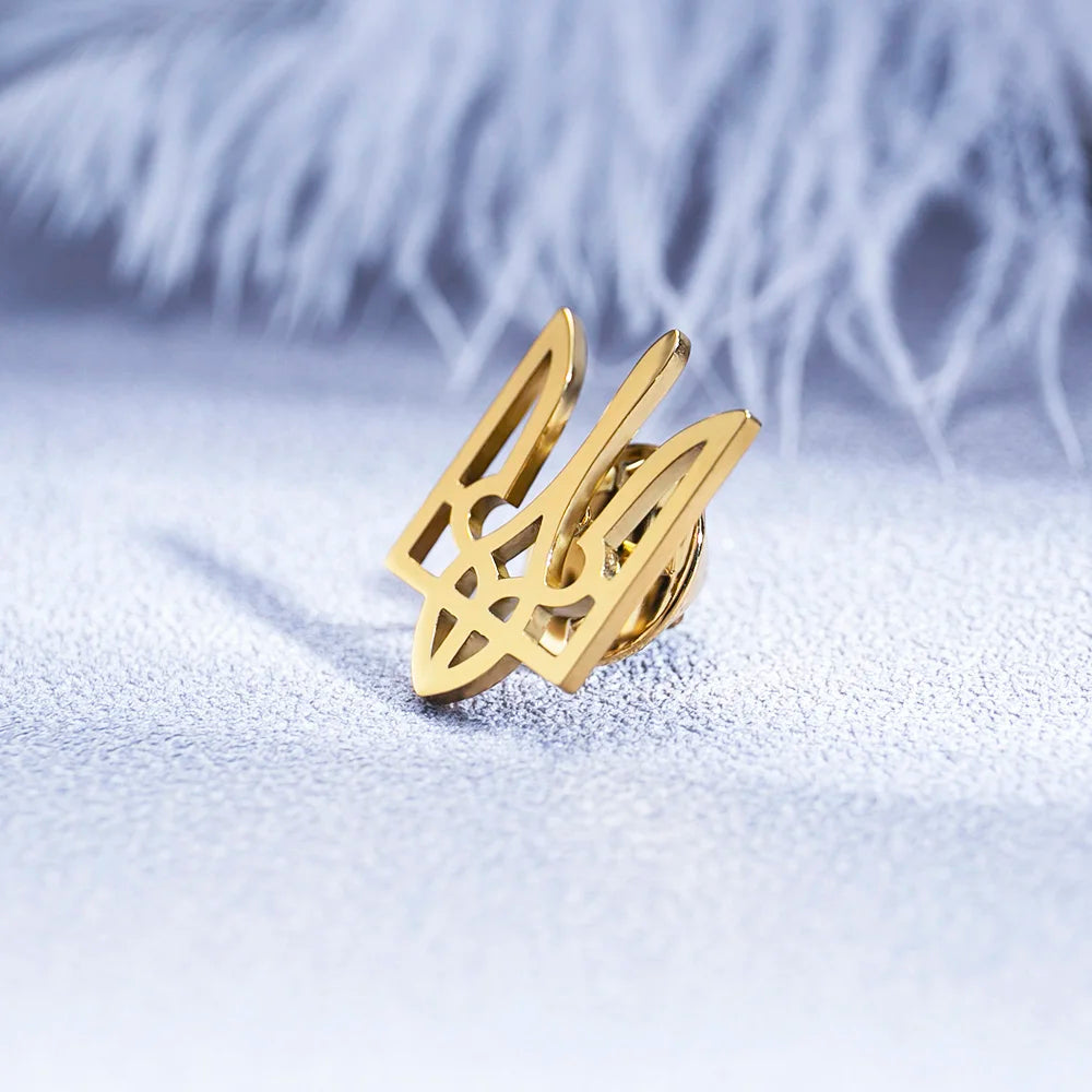 Elegant golden Ukrainian Tryzub brooch on soft textured background, made of high-quality stainless steel for stylish occasions.