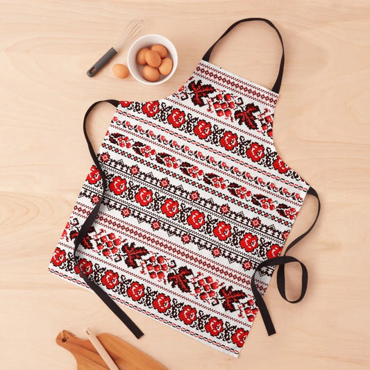 Ukrainian embroidered pattern apron with red and black design, adjustable straps, displayed on a kitchen table with eggs and utensils.