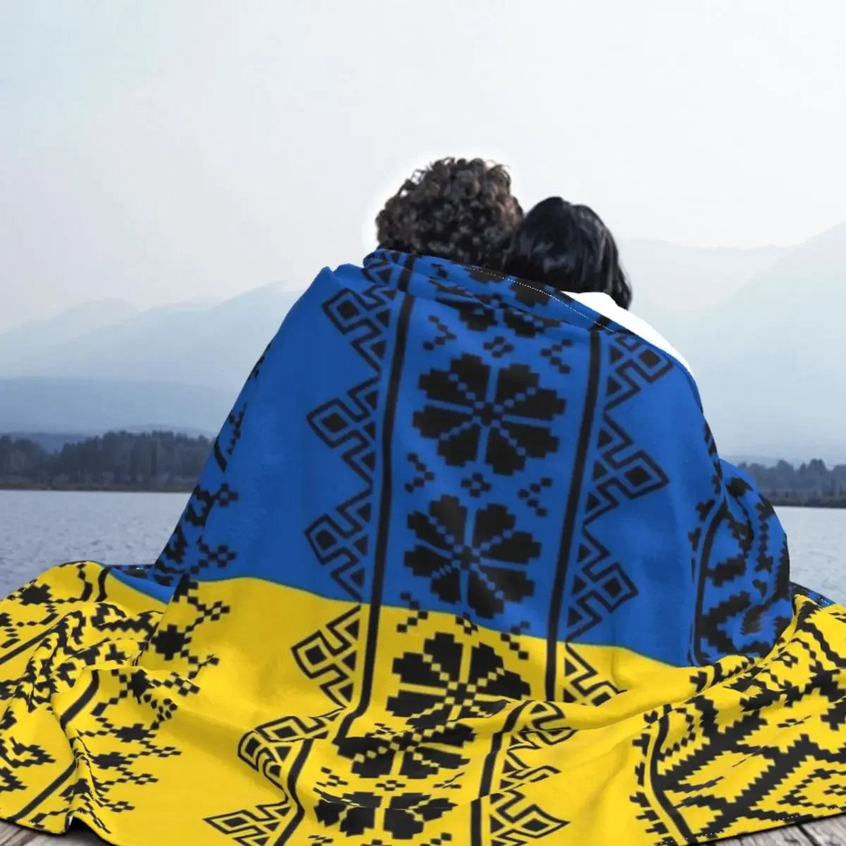 Couple wrapped in Ukrainian Vyshyvanka flannel blanket with embroidered patterns by a serene lakeside.