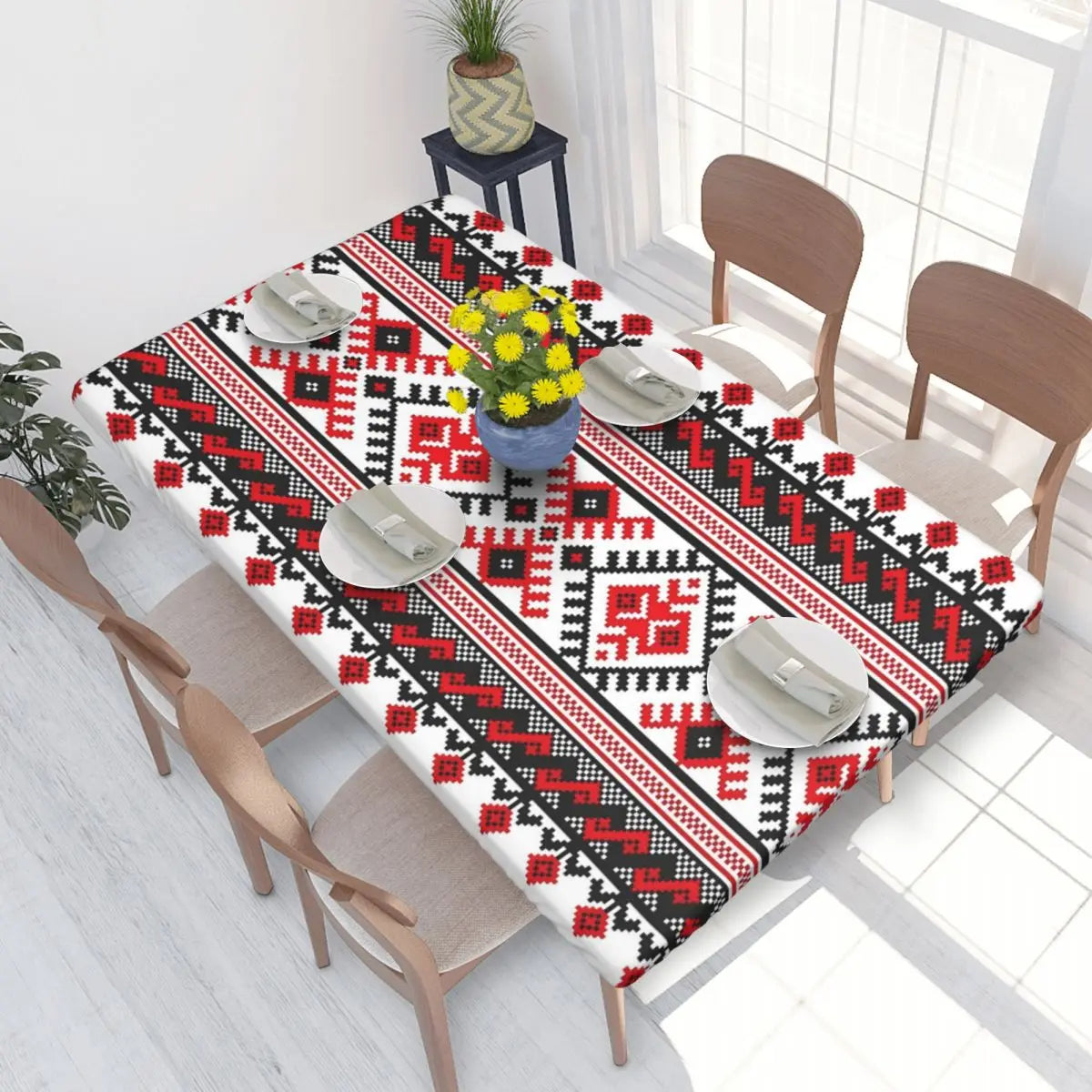 Ukrainian embroidery table cover with red and black patterns on dining table, set with plates and a vase.