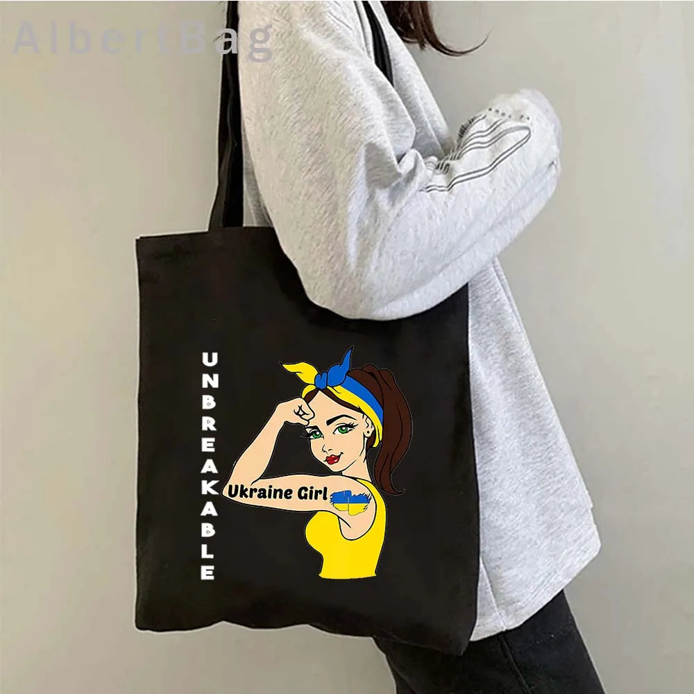 Ukrainian Patriotic Grocery Tote Bag with "Unbreakable Ukraine Girl" print, held by person wearing gray sweatshirt.