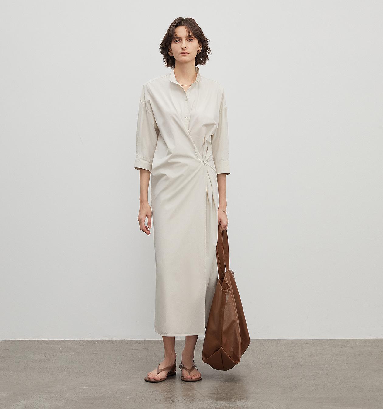 Woman wearing Origami Trace Wrap Dress in high-density cotton with stand collar and wrap silhouette, holding a brown bag.