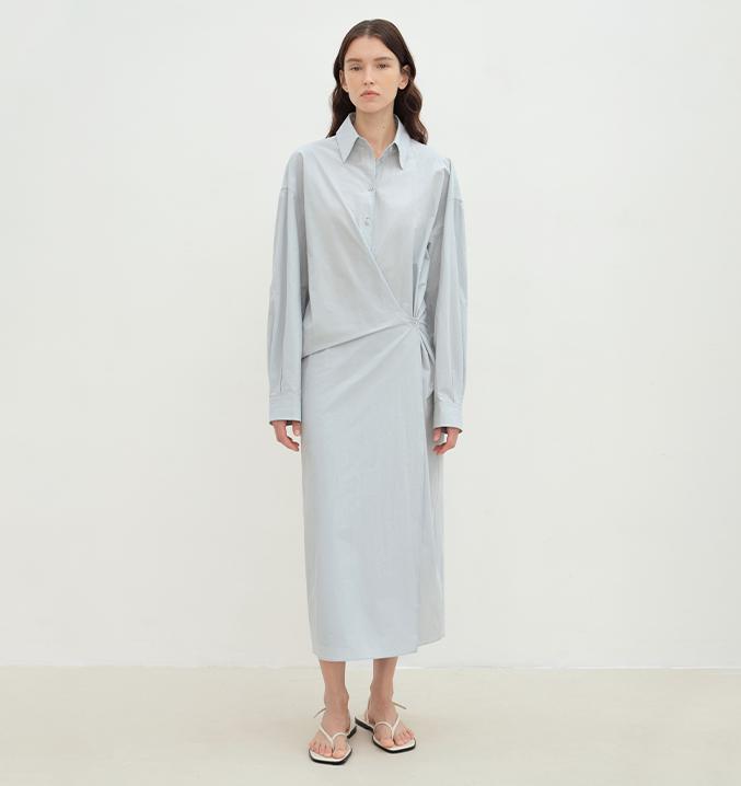 Woman wearing Whisper Wrap Cotton Shirt Dress with cocoon silhouette, refined lapel collar, and cross-placket closure in light blue.
