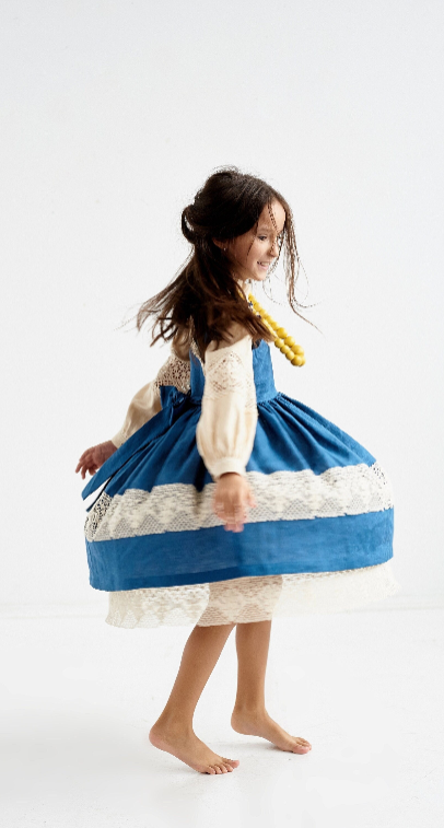 Young girl spinning in a vintage blue dress with lace details, enjoying playful movement in a bright space.