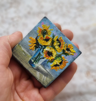 Hand holding a miniature canvas painting of vibrant yellow sunflowers in a blue vase, showcasing detailed and colorful artistry.