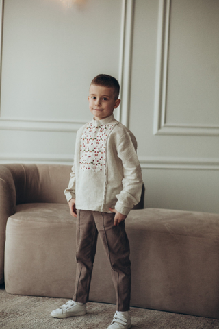 Young boy in stylish outfit standing by a sofa in a modern living room.