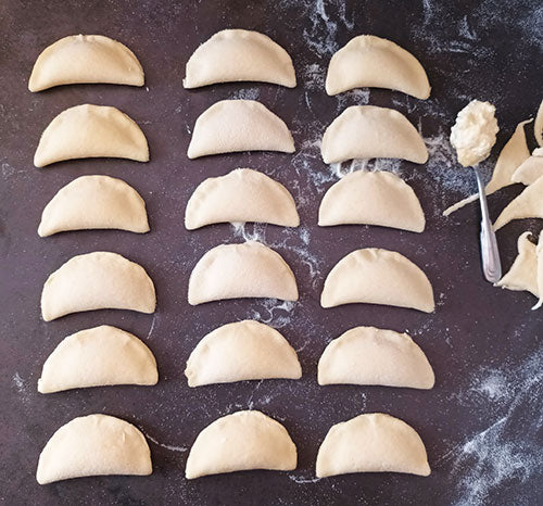 Rows of handmade Ukrainian varenyky dumplings arranged on a table, ready to be filled with potato, cabbage, or farmer's cheese.