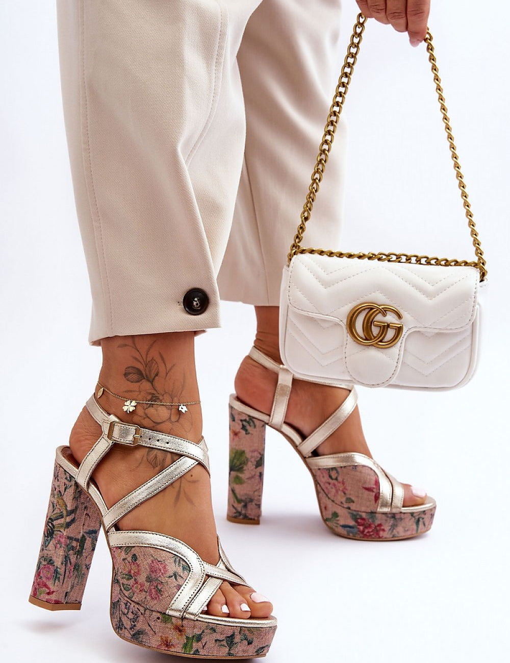 Fashion-forward leather platform heel sandals with floral design worn by a model holding a white designer handbag.