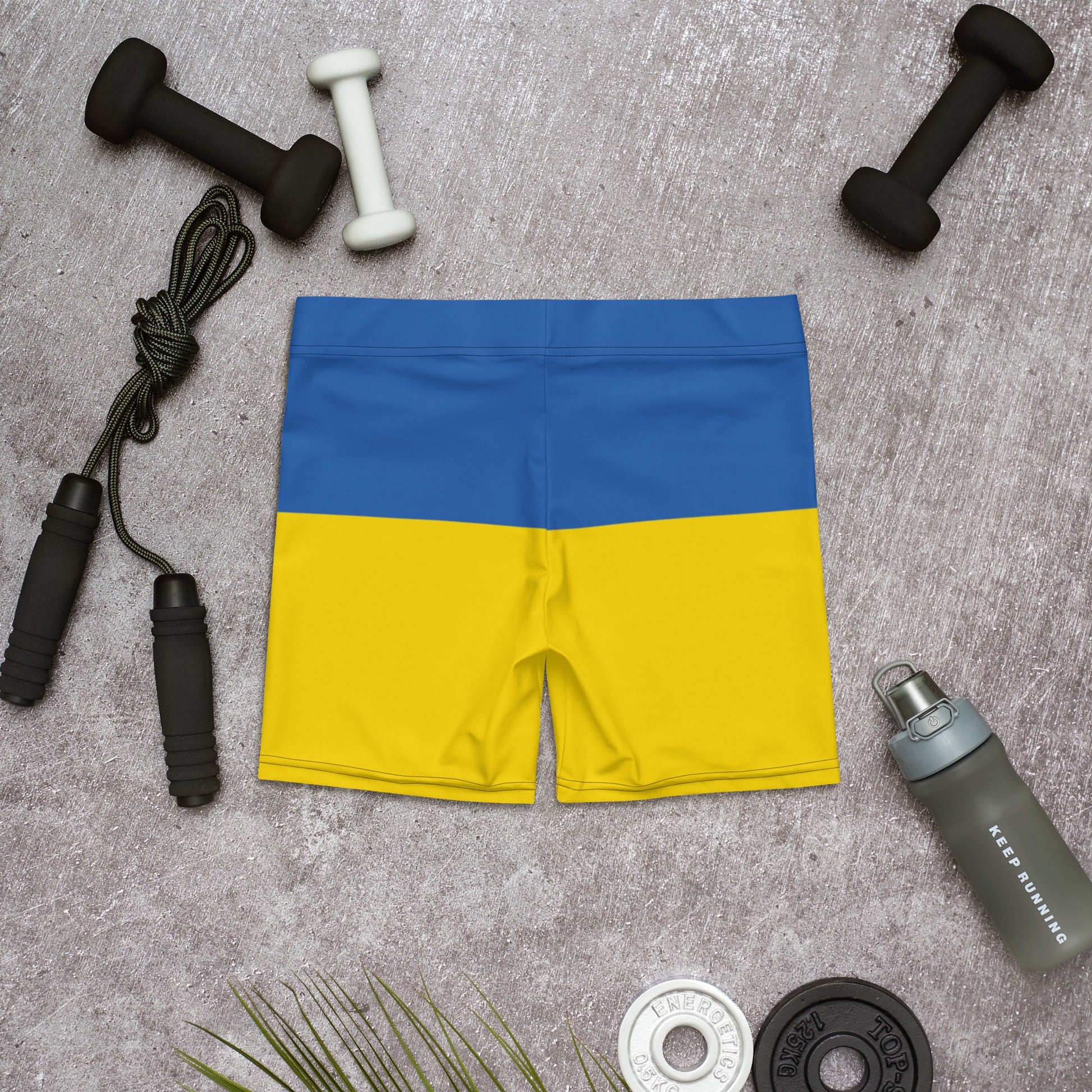 Ukrainian Flag shorts featuring blue and yellow design, ideal for workouts. Set against a gym-themed background with dumbbells and jump rope.