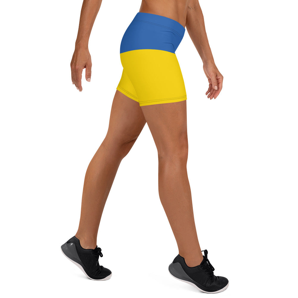 Woman wearing Ukrainian Flag shorts with blue and yellow design, part of the Ukrainian Vibe Trizub Collection, side view.