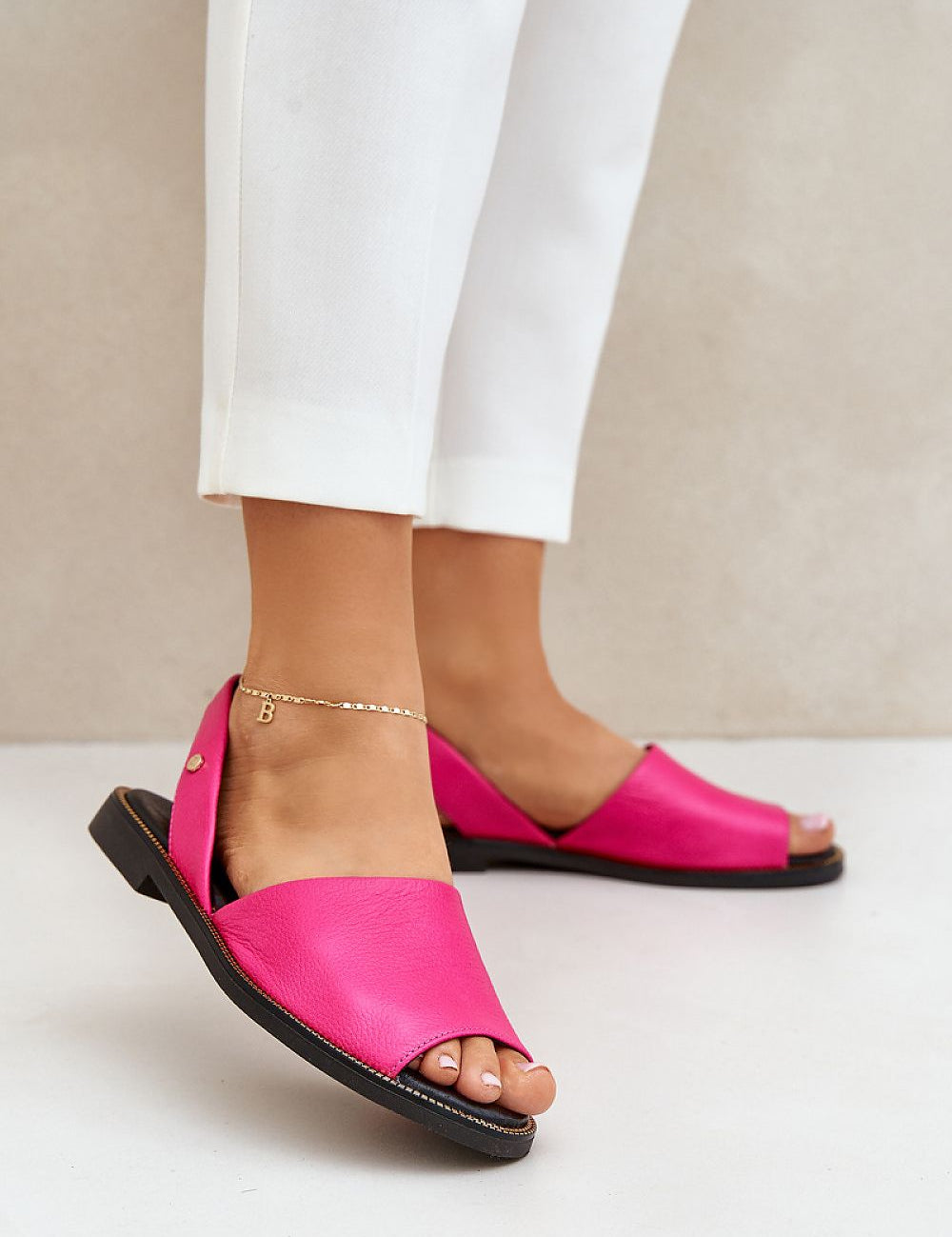 Woman wearing pink Alviera leather slip-on flat sandals with open toe design and flat heel, paired with white pants.