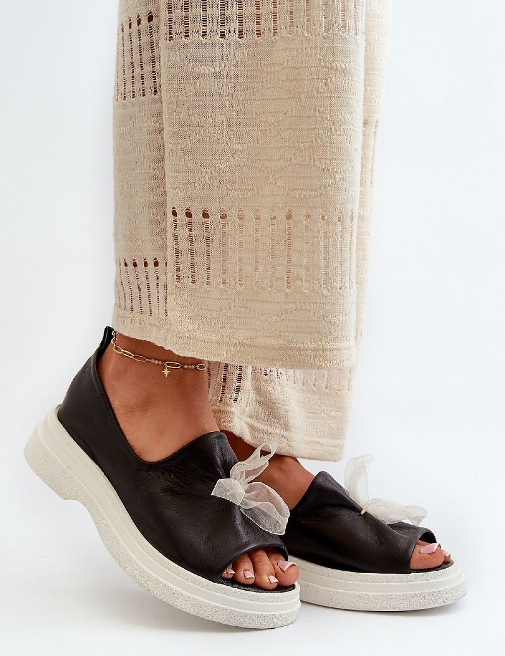 Woman wearing Alvion Bow Leather Platform Sandals with bow detail and thick sole, paired with cream pants, showcasing summer style.