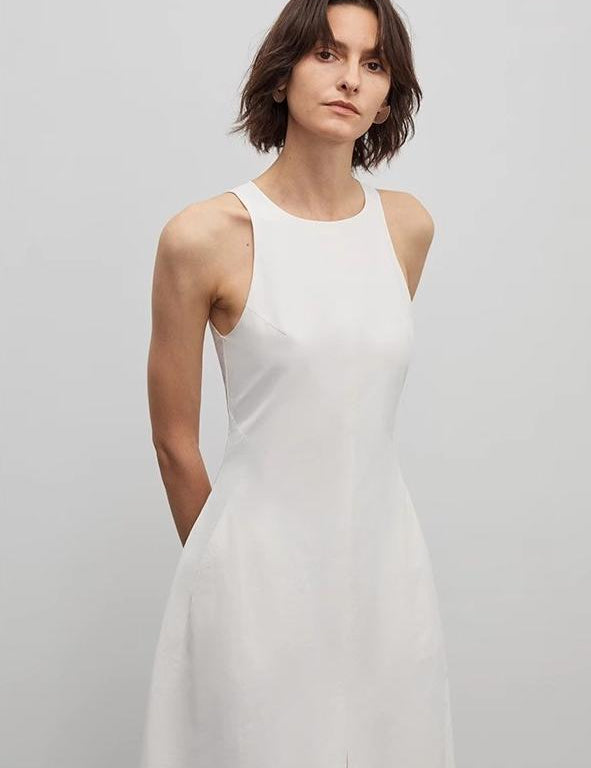Woman in white sleeveless A-line dress by Arclaire, showcasing minimalist French elegance and architectural design.