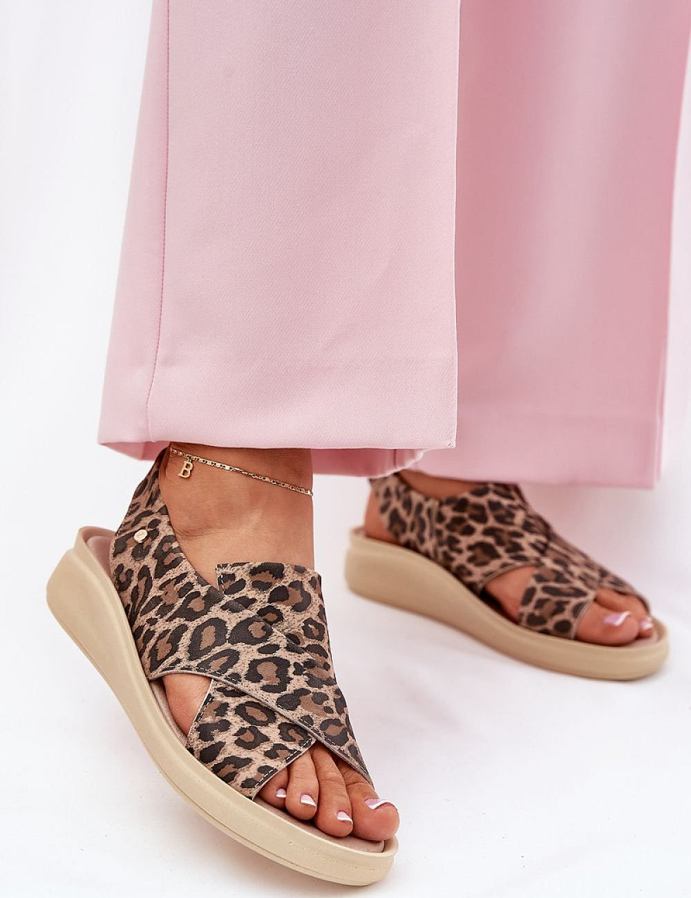 Woman wearing Arlienne Leather Platform Slip-On Sandals with leopard pattern, paired with pink pants for stylish comfort and height.