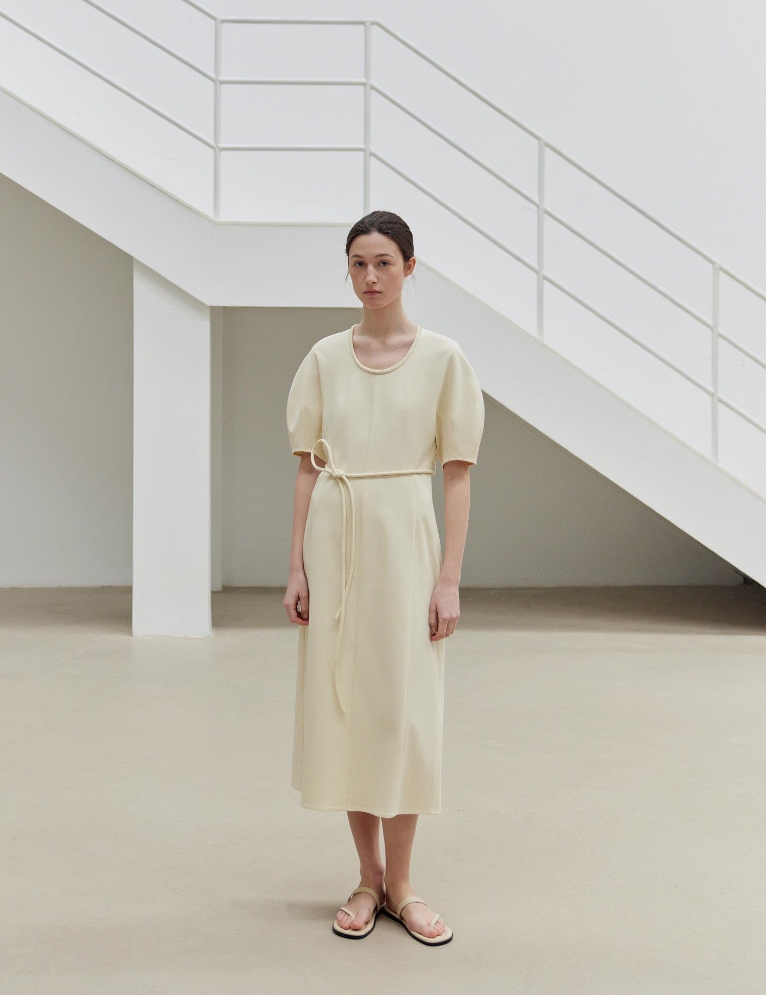 Model wearing Aurelia Cotton Rope Knit Dress in cream, showcasing relaxed tailoring and curved skirt for elegant movement.