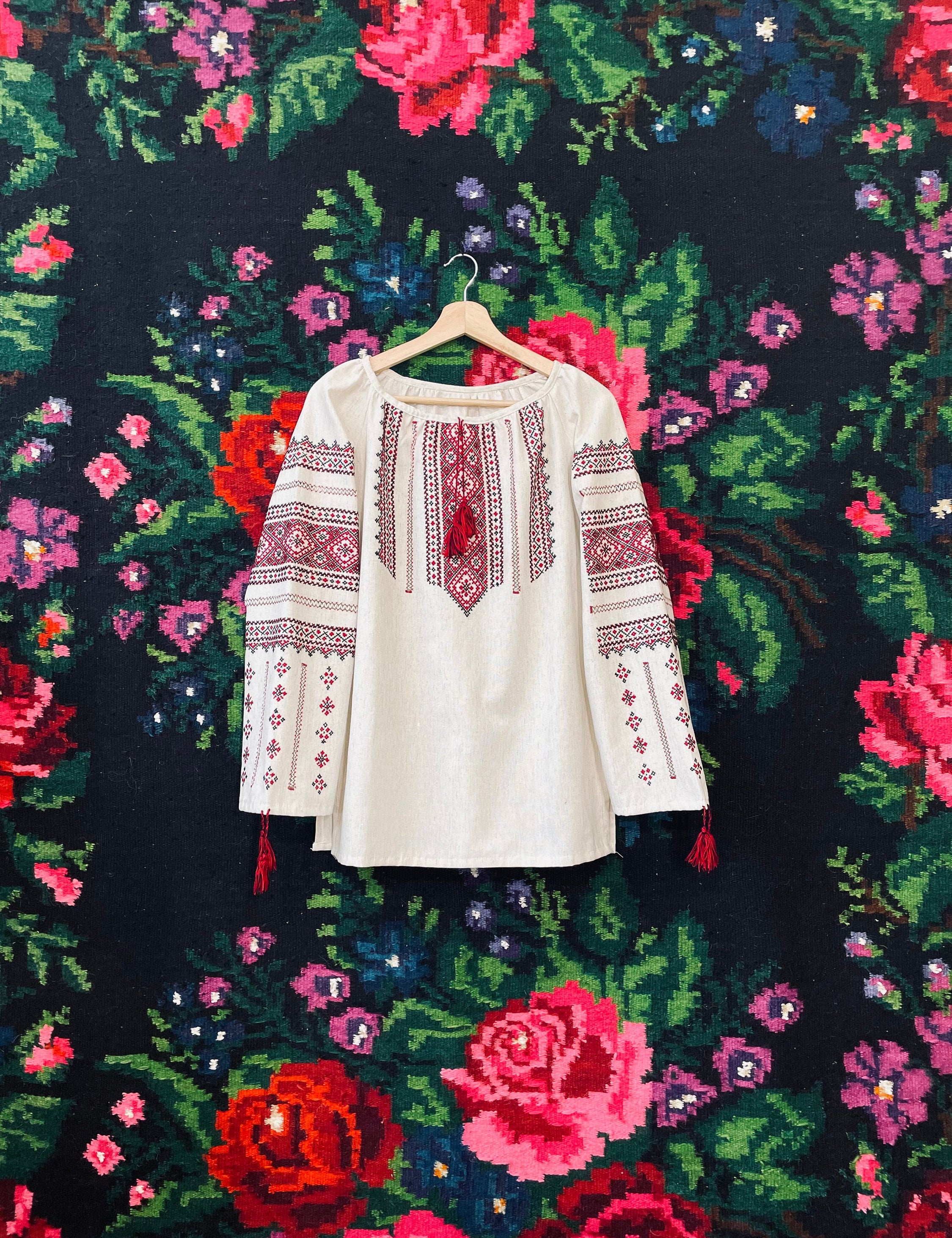 Authentic Ukrainian Vyshyvanka blouse with intricate embroidery, hanging against a vibrant floral background.