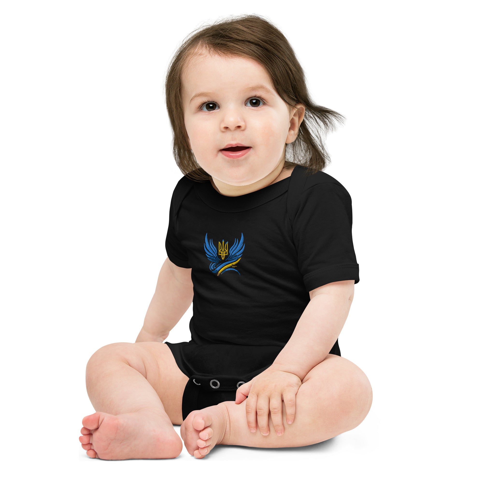 Baby wearing black short sleeve one piece with Ukrainian Tryzub logo, sitting happily on the floor.