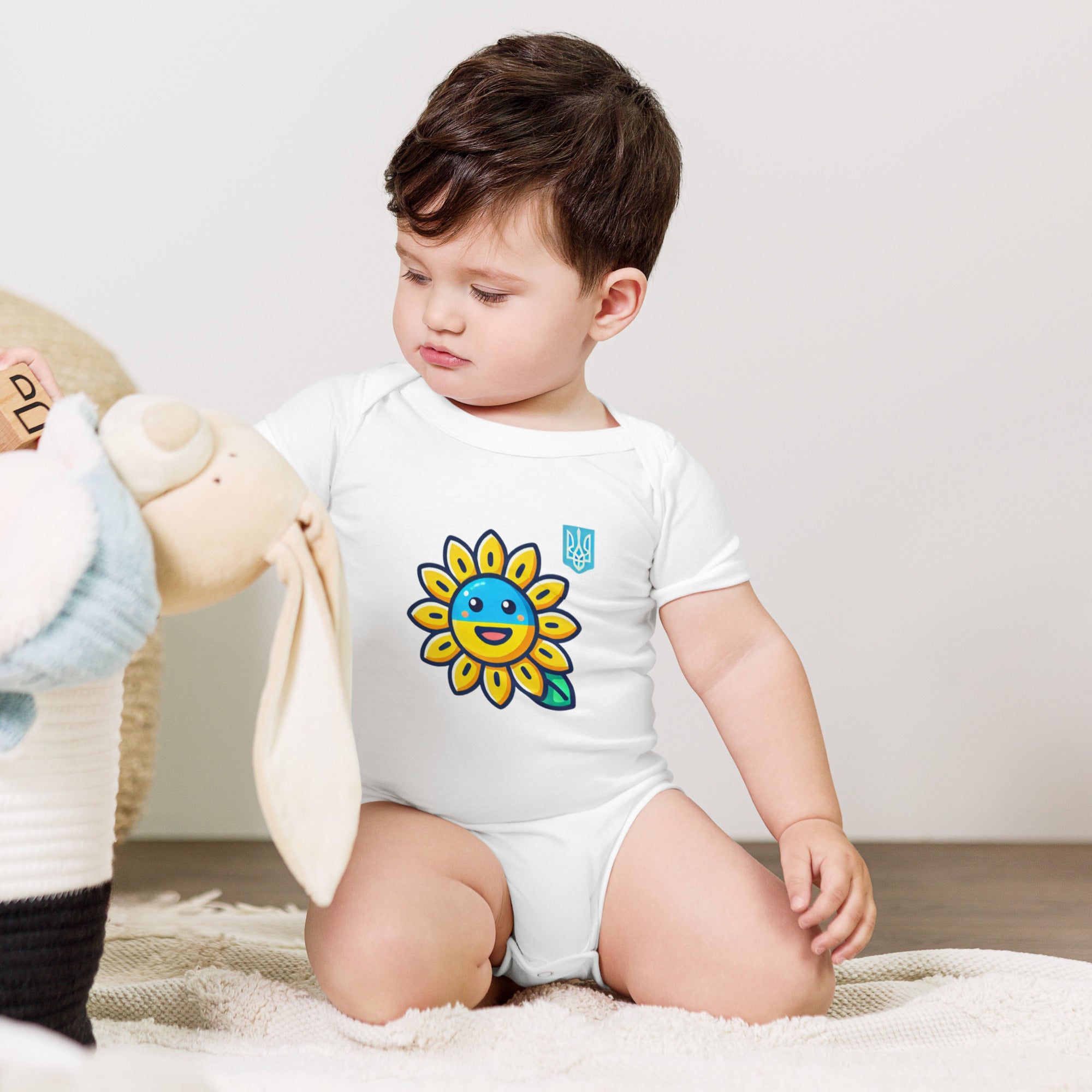 Baby wearing sunflower and Ukrainian flag bodysuit sitting on floor with toys.