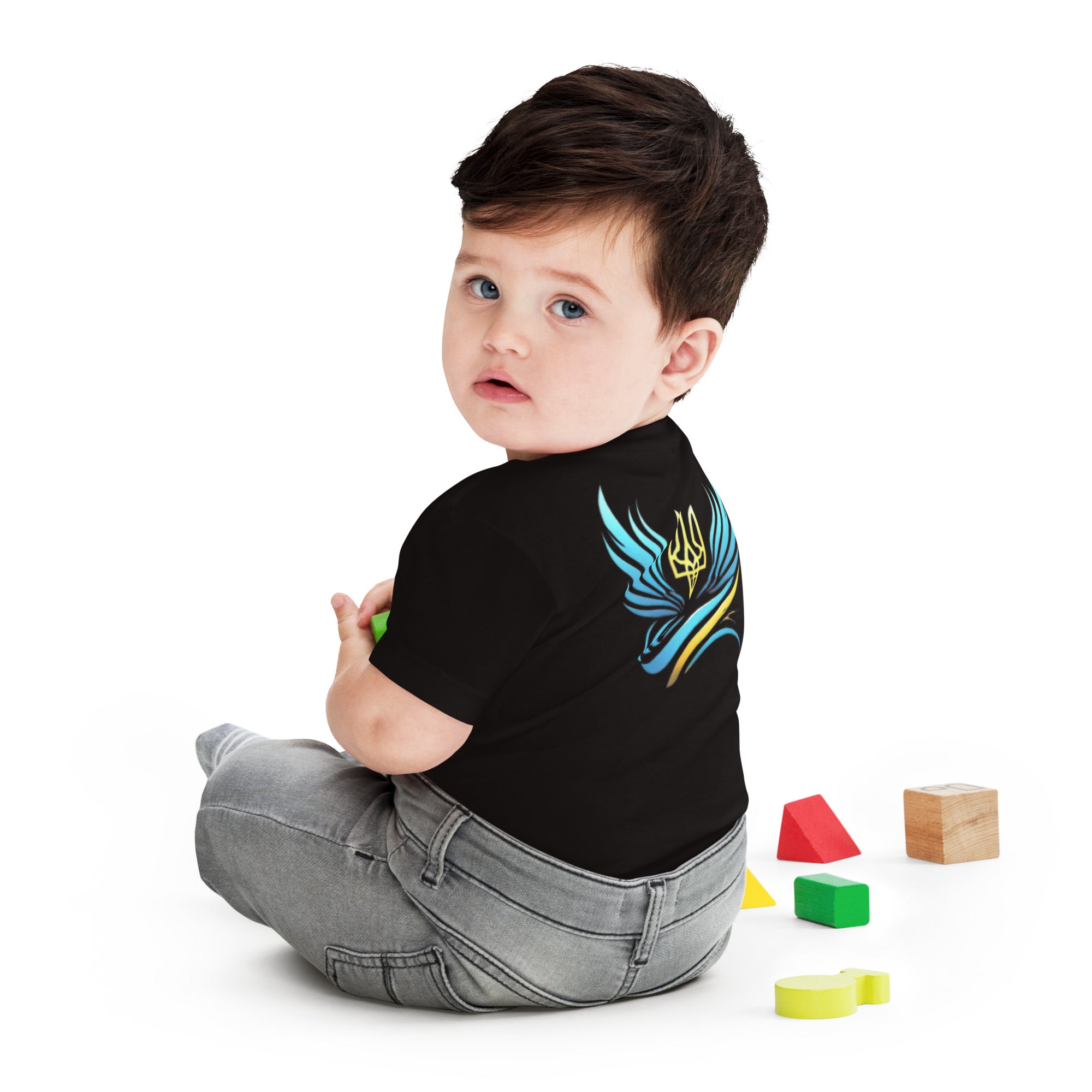 Baby wearing black jersey tee with Ukrainian symbol, sitting with colorful toy blocks.
