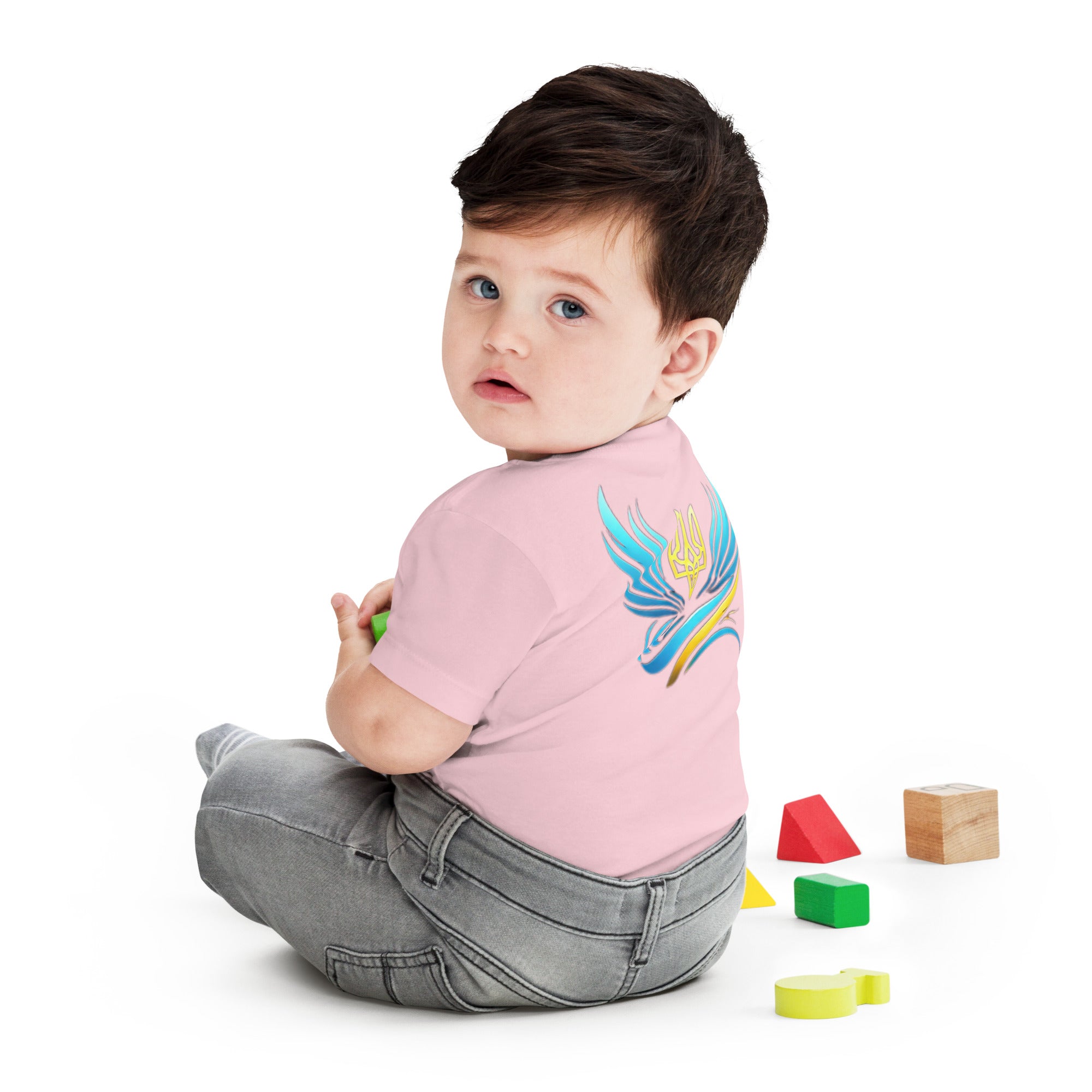 Baby wearing pink jersey tee with Ukrainian symbols, sitting on floor with colorful blocks.