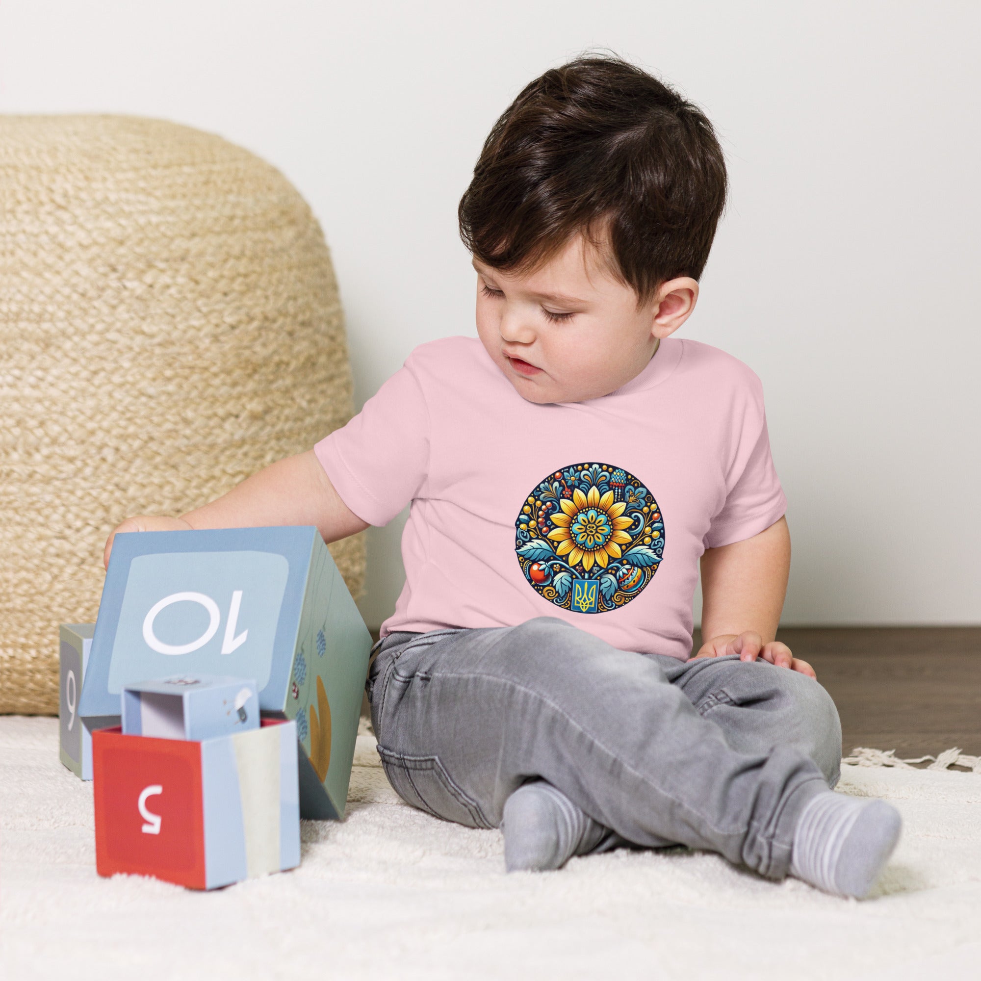Baby in jersey tee with Ukrainian symbol design, playing with blocks.