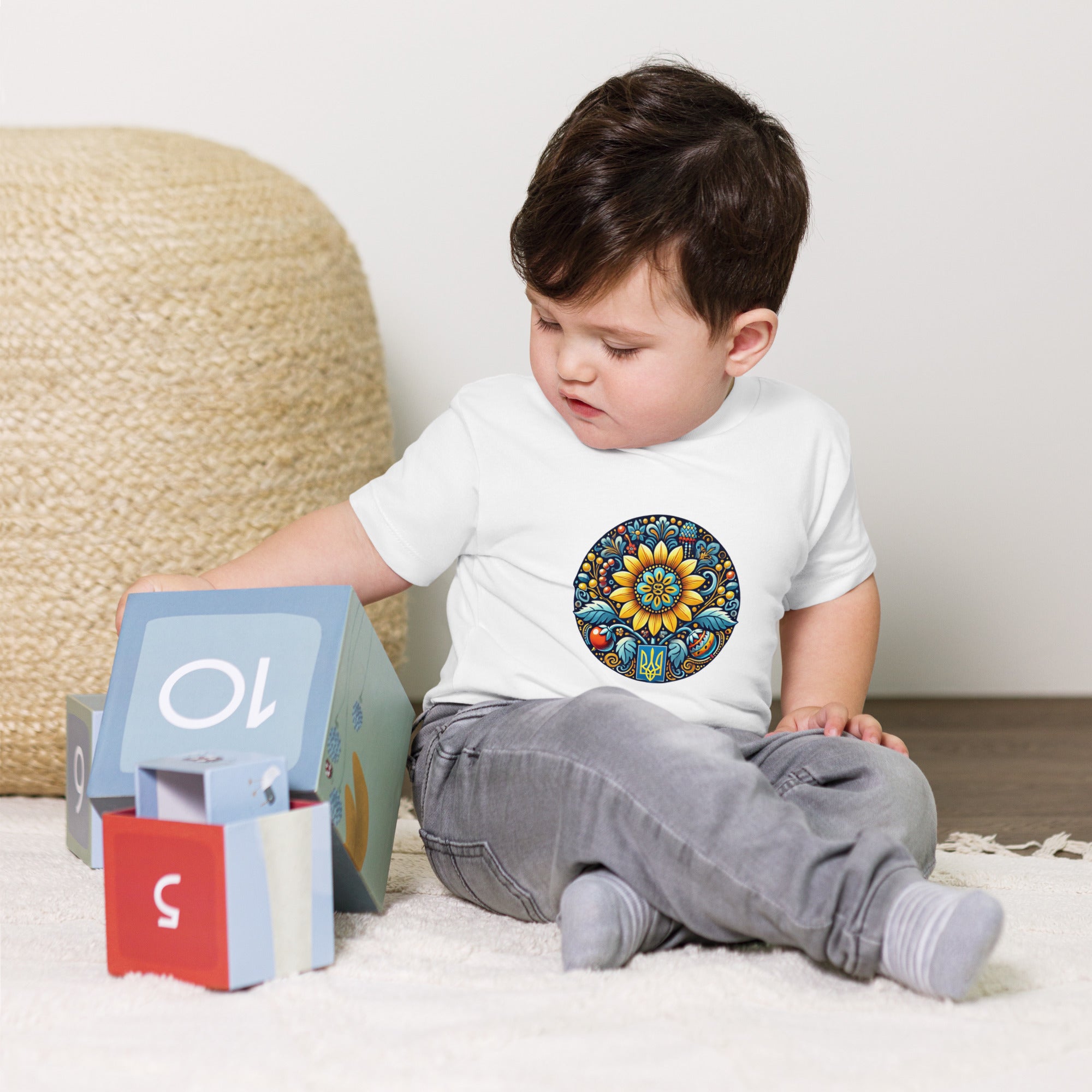 Toddler wearing baby jersey tee with Ukrainian symbols, playing with blocks.