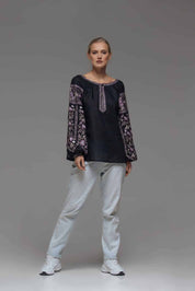 Woman wearing black linen embroidered Ukrainian vyshyvanka blouse with symbolic back ornament and intricate sleeve designs.