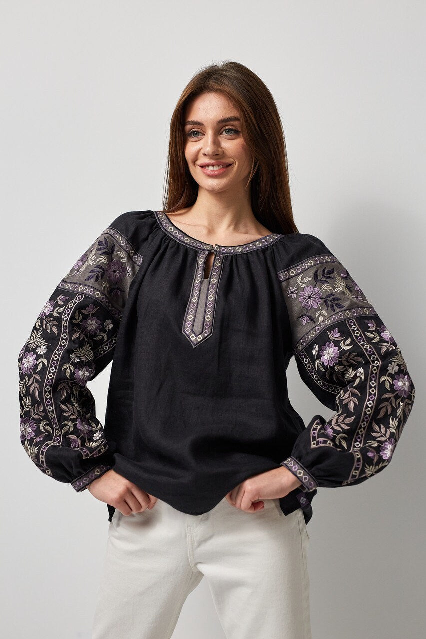 Woman wearing black linen embroidered Ukrainian vyshyvanka blouse with symbolic back ornament, featuring traditional floral patterns.
