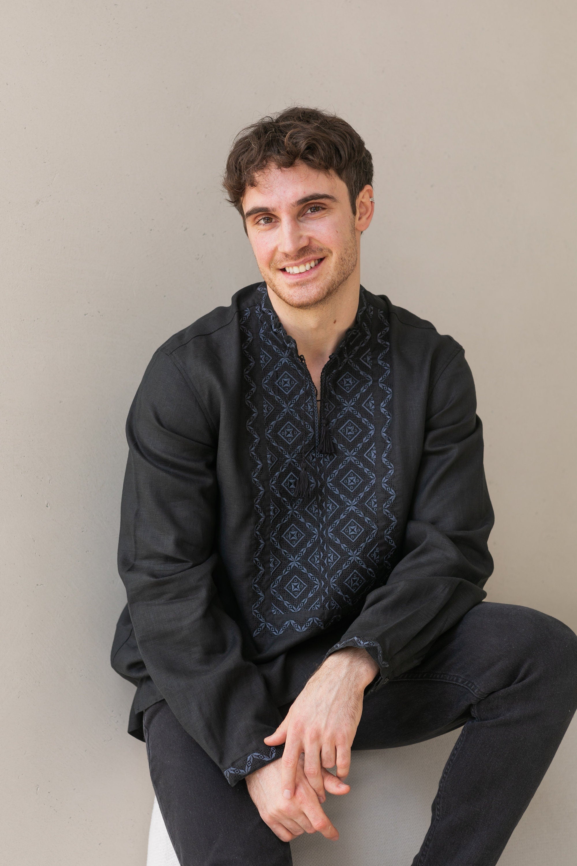 Man wearing a black linen Ukrainian Vyshyvanka shirt with traditional Poltava embroidery, sitting against a neutral background.