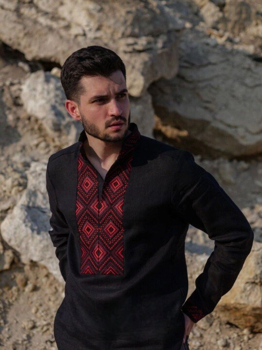 Black linen men's shirt with red geometric embroidery, Ukrainian Vyshyvanka, worn by a model outdoors against a rock backdrop.