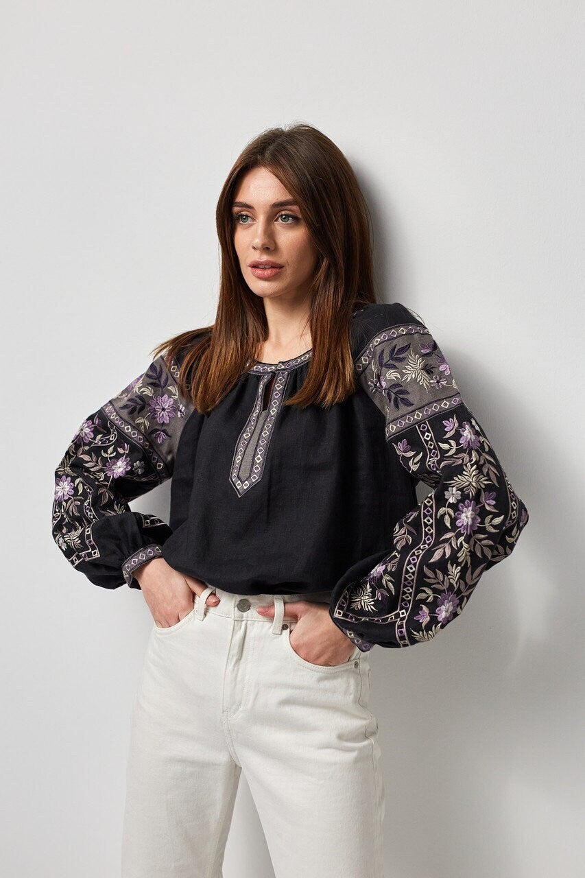 Woman wearing black linen embroidered blouse with Ukrainian vyshyvanka design, featuring traditional symbolism and modern aesthetics.