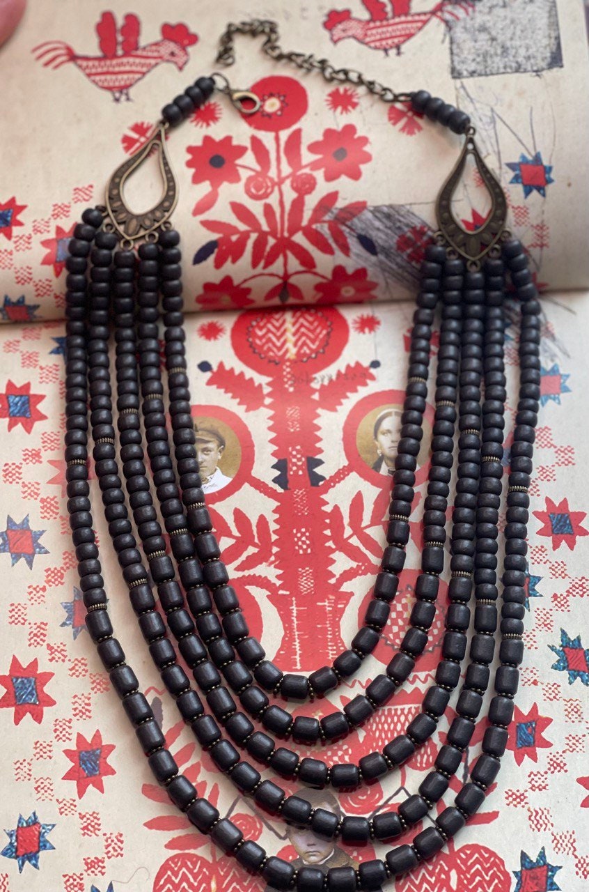 Handmade black ceramic Ukrainian necklace with Hutsul ethnic style on traditional red and white patterned background.