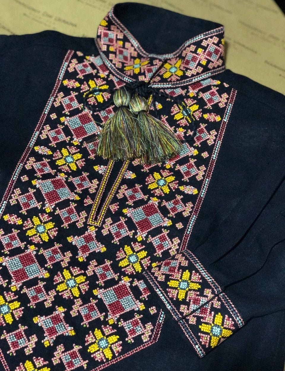 Close-up of a traditional Ukrainian vyshyvanka with intricate colorful embroidery and tassels on a dark fabric.