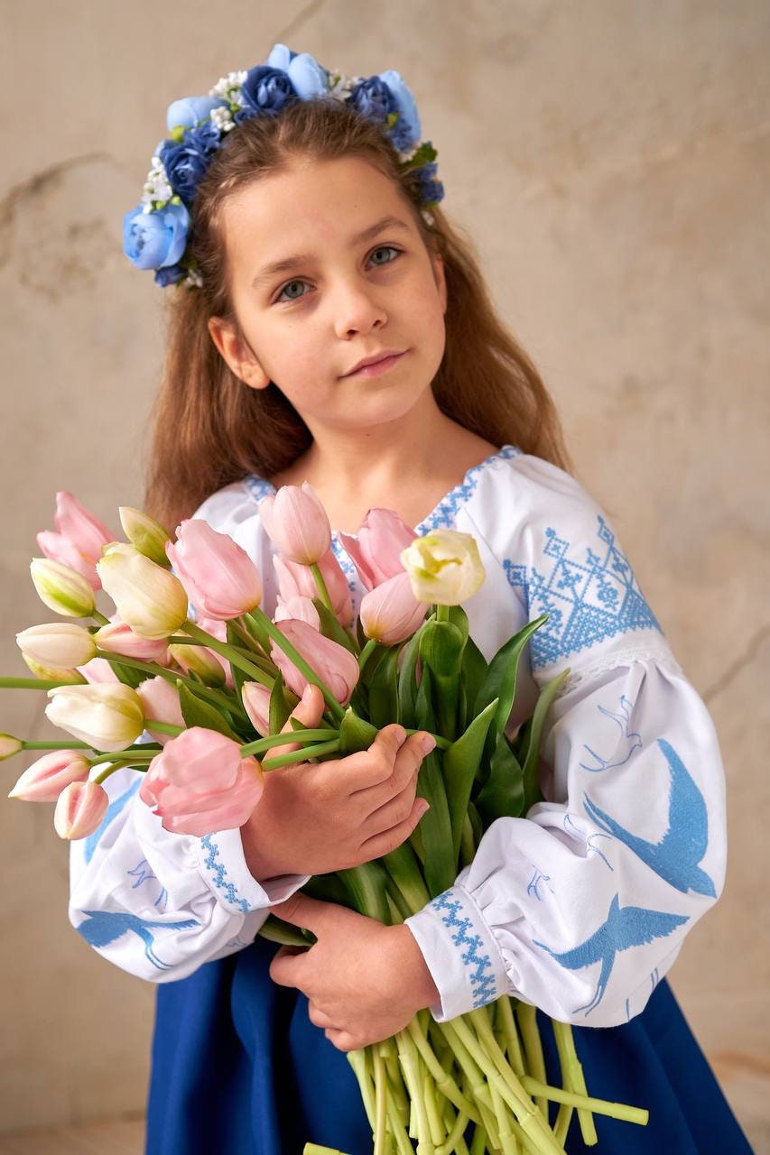 Girl wearing a Ukrainian blouse with blue and yellow embroidery, holding tulips, symbolizing peace and cultural heritage.
