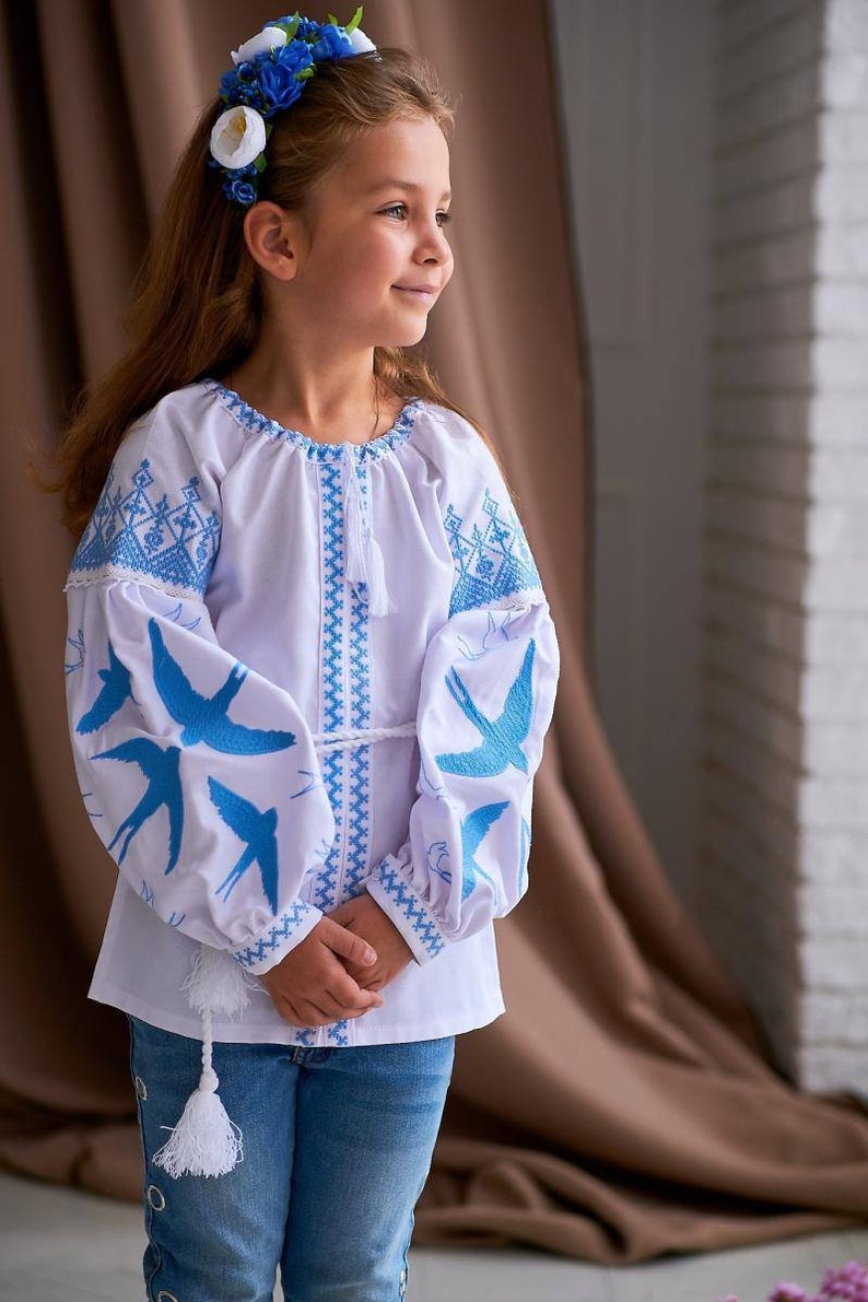Girl wearing blue and yellow embroidered blouse with Ukrainian swallow design, symbolizing peace and freedom.
