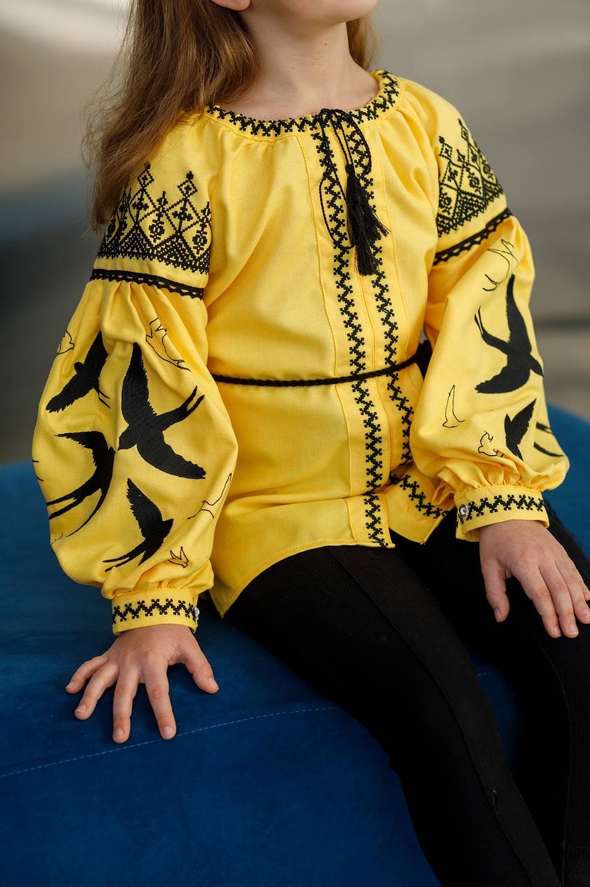 Girl wearing a yellow Ukrainian blouse with blue swallow embroidery, symbolizing peace and freedom, for festive or everyday wear.