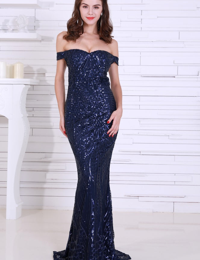 Woman wearing Aurélia Navy Sequin Evening Gown with off-shoulder design and fitted silhouette against a white background
