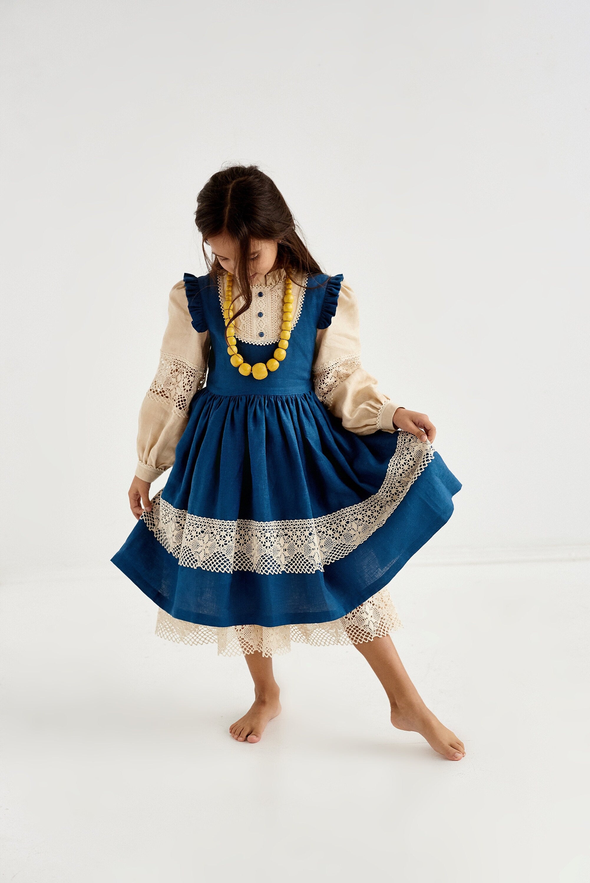 Girl wearing blue Ukrainian linen dress with lace trim, long puff sleeves, decorative necklace. Perfect for special occasions.