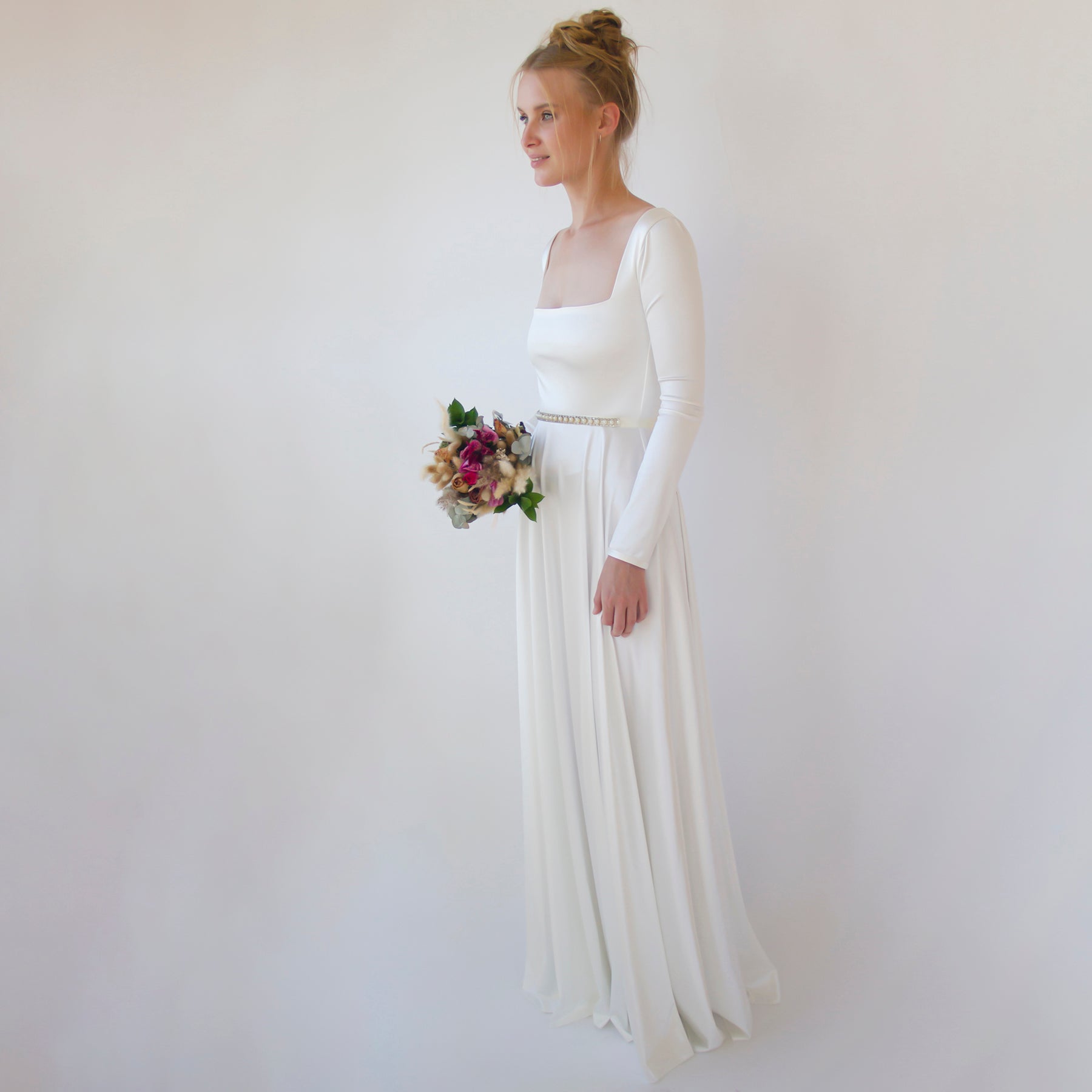 Bride wearing Céleste Vintage Pearl Sash Belt with crystal rhinestones and pearly beads on a white dress, holding a bouquet.