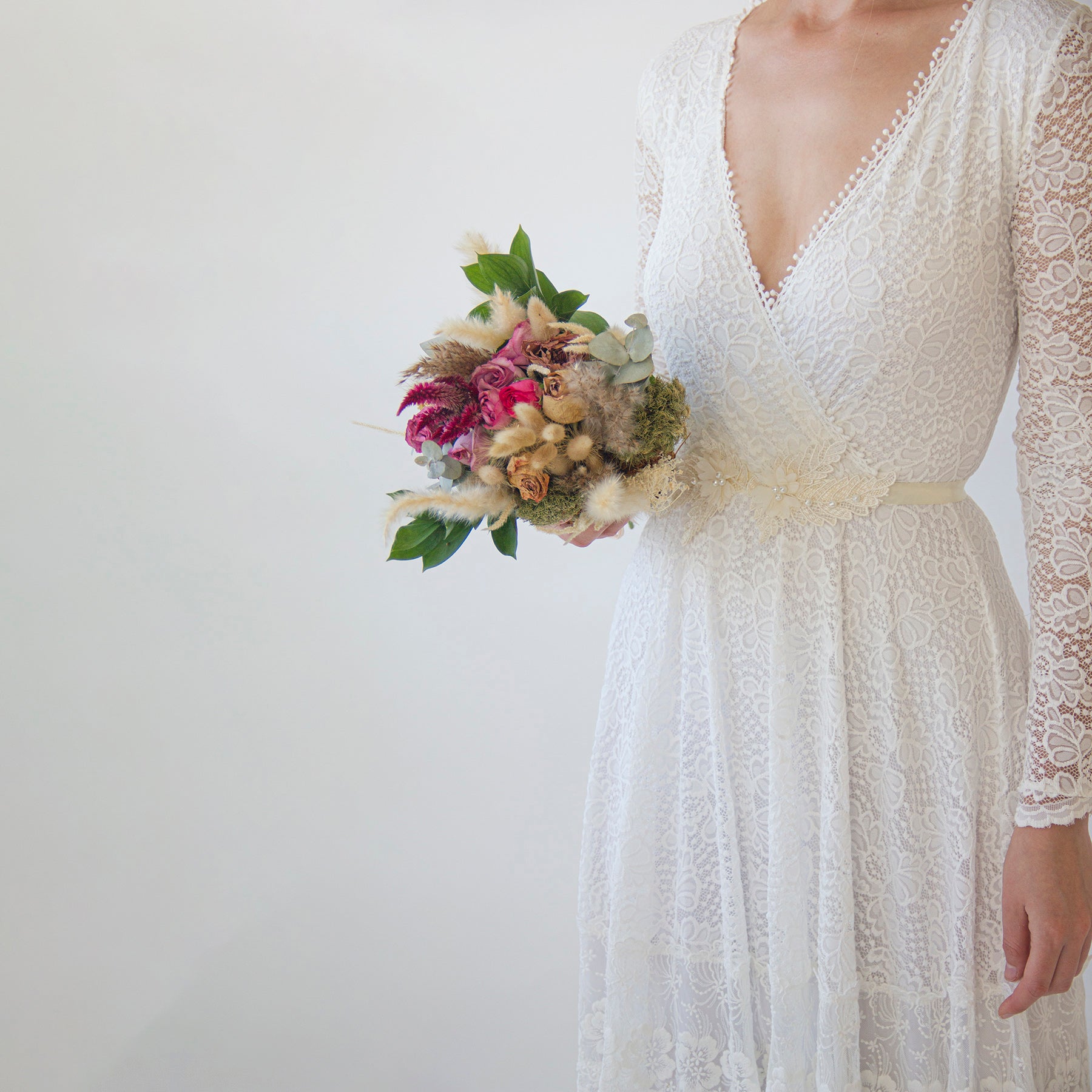 Bride wearing lace gown with Isara Beaded Floral Sash, holding a bouquet, showcasing elegant bridal fashion.