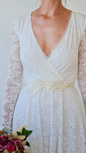 Bride wearing Isara Beaded Floral Sash with lace dress, showcasing elegant floral lace and beaded details, holding bouquet.