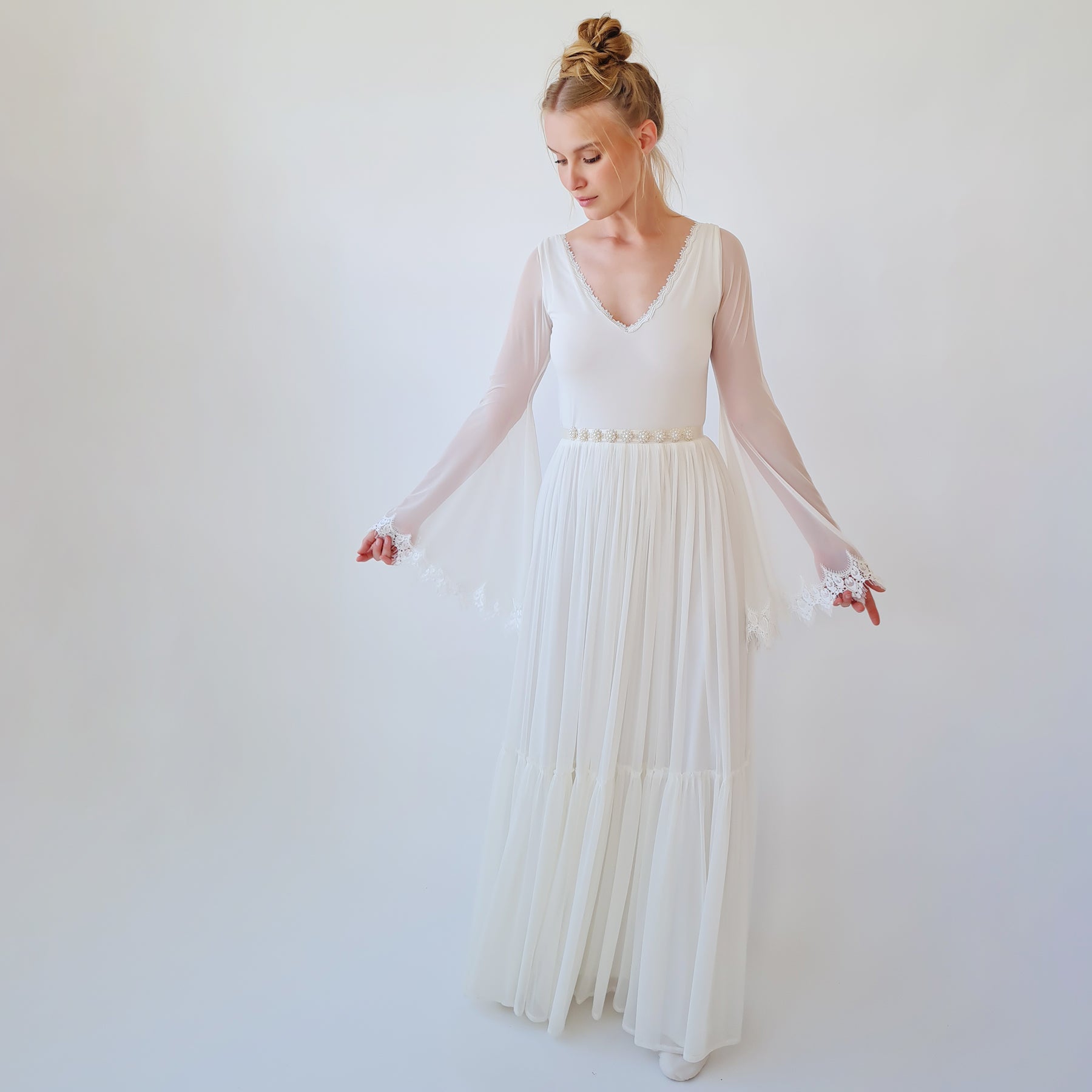 Bridal gown with sheer long sleeves and flowing skirt, featuring a delicate sash with hand-applied beads and satin ribbon ties.
