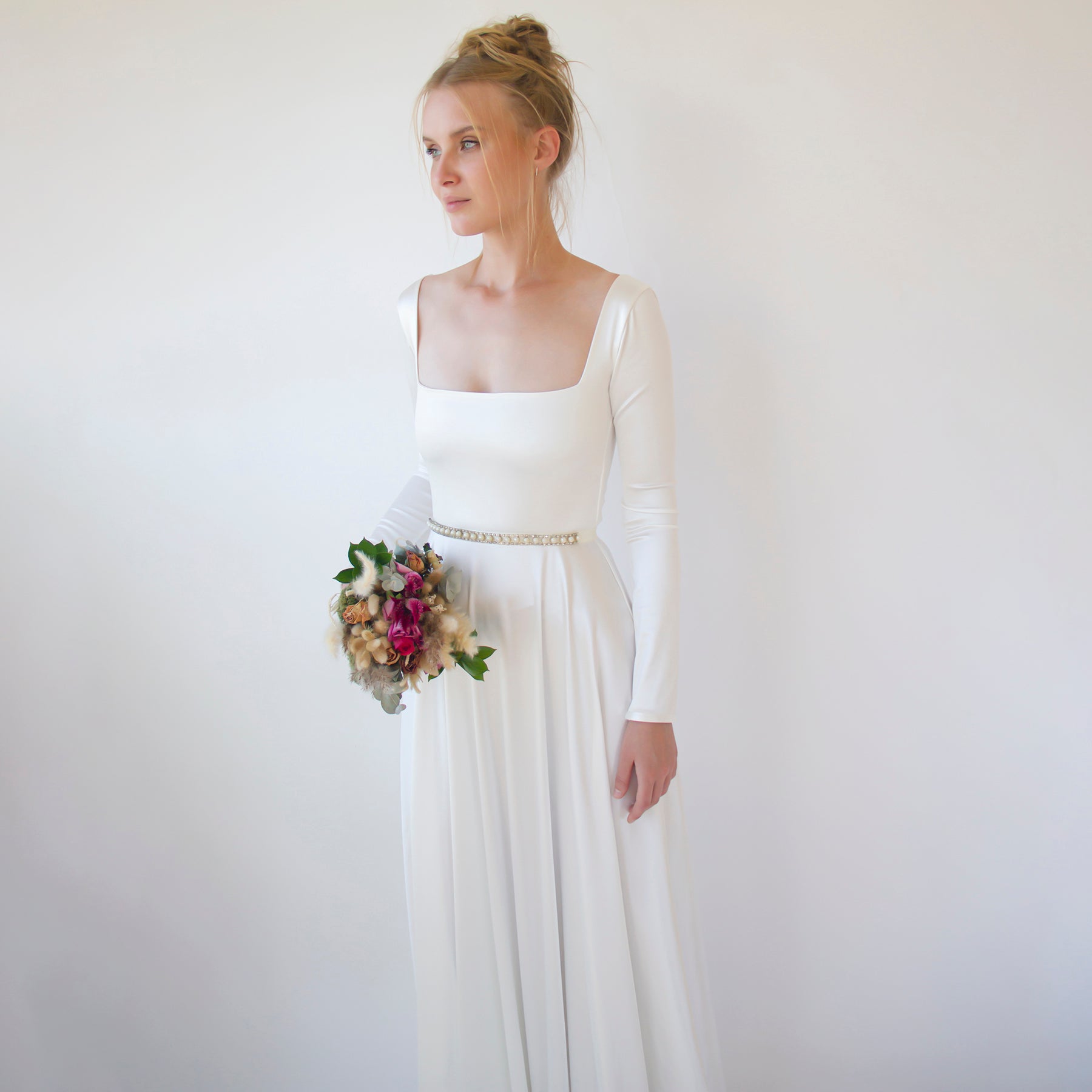 Bride in white gown wearing Céleste Vintage Pearl Sash Belt, holding bouquet, exuding elegance and grace.