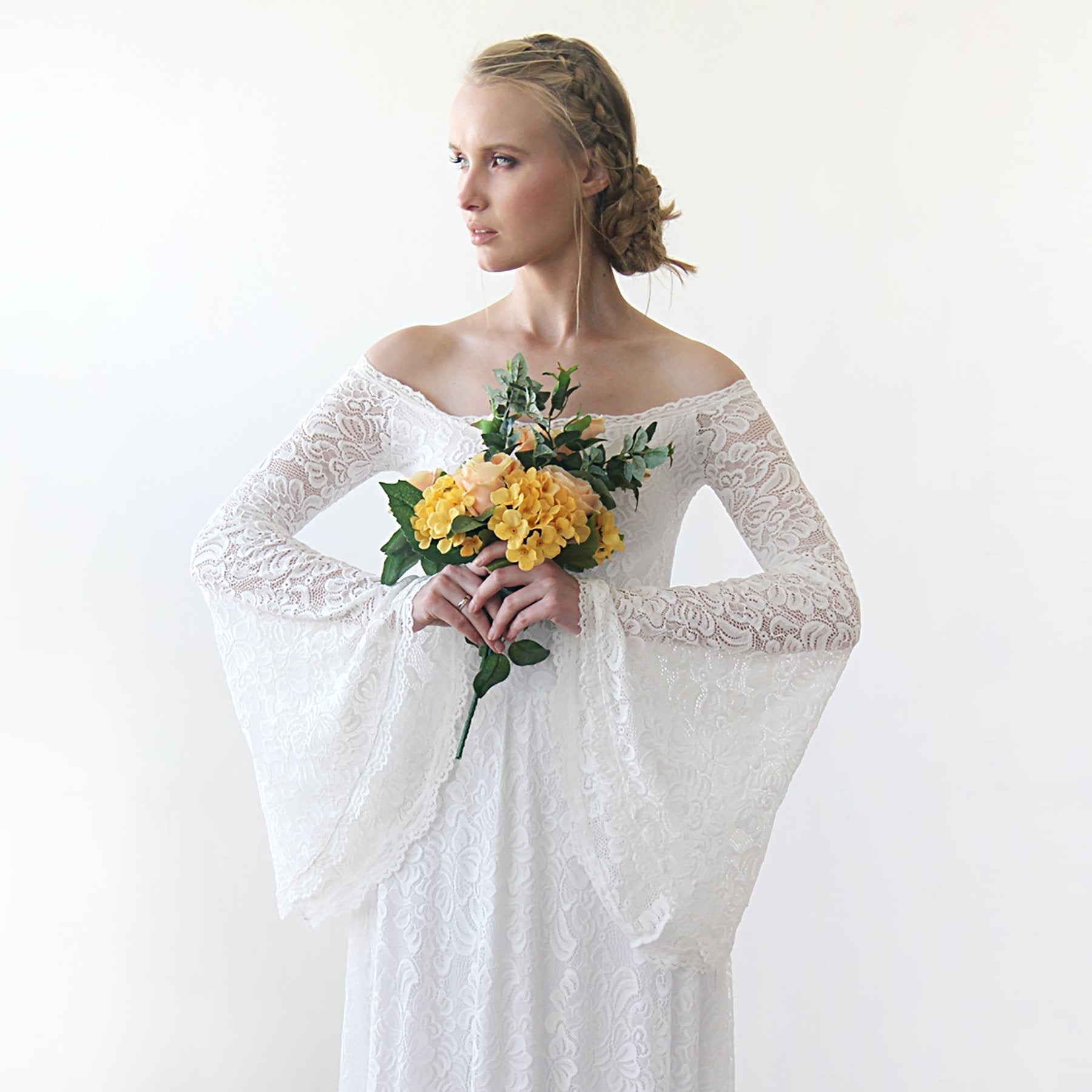 Bride in an ivory off-shoulder Lirienne wedding dress with lace bell sleeves, holding a bouquet of yellow flowers.