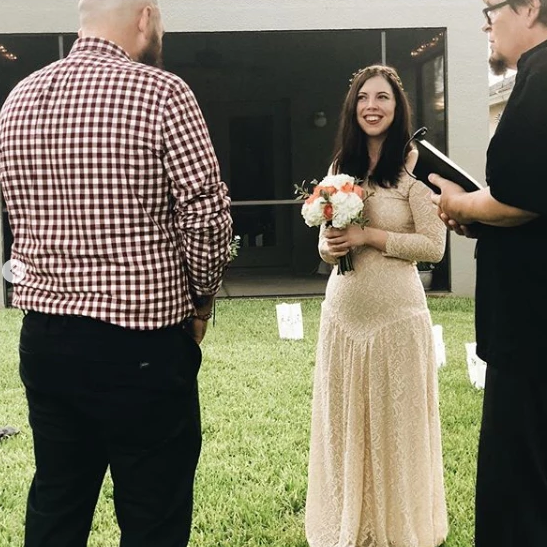 Bride in medieval lace wedding dress holding a bouquet during an outdoor ceremony