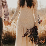 Woman in lace wedding dress holding bouquet, standing in field during golden hour, showcasing rustic elegance and romantic style.
