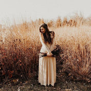 Bride wearing Elverin Medieval Lace Wedding Dress in a field, showcasing off-the-shoulder neckline and romantic lace sleeves.