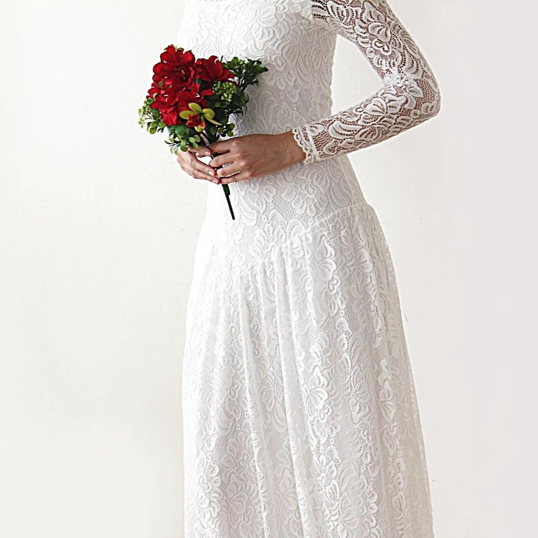 Bride wearing a lace medieval-style wedding dress holding a bouquet of red flowers, showcasing elegant bridal fashion.